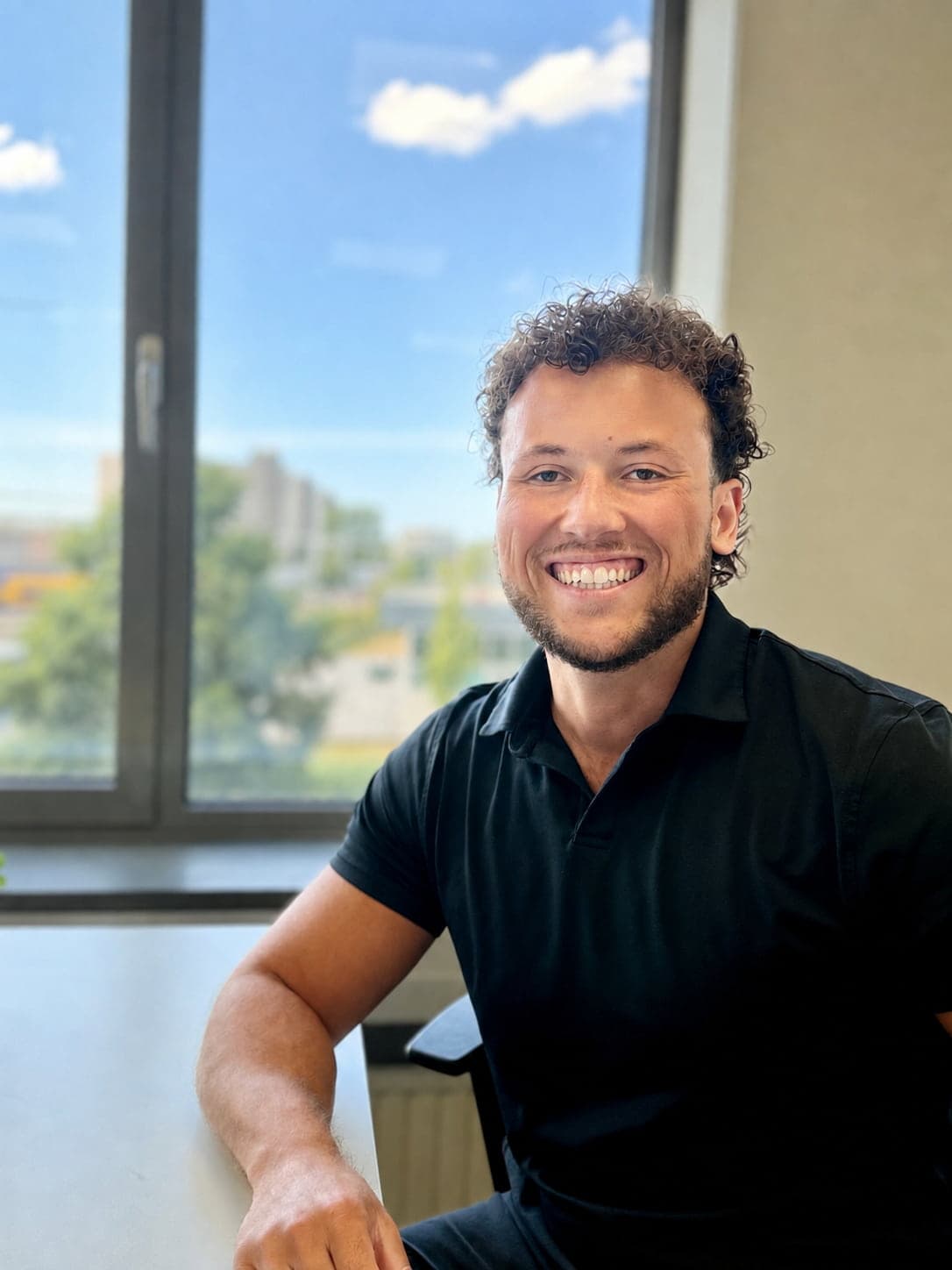 Founder of DominicanVest smiling sitting down on a chair with a window in the background blurred out